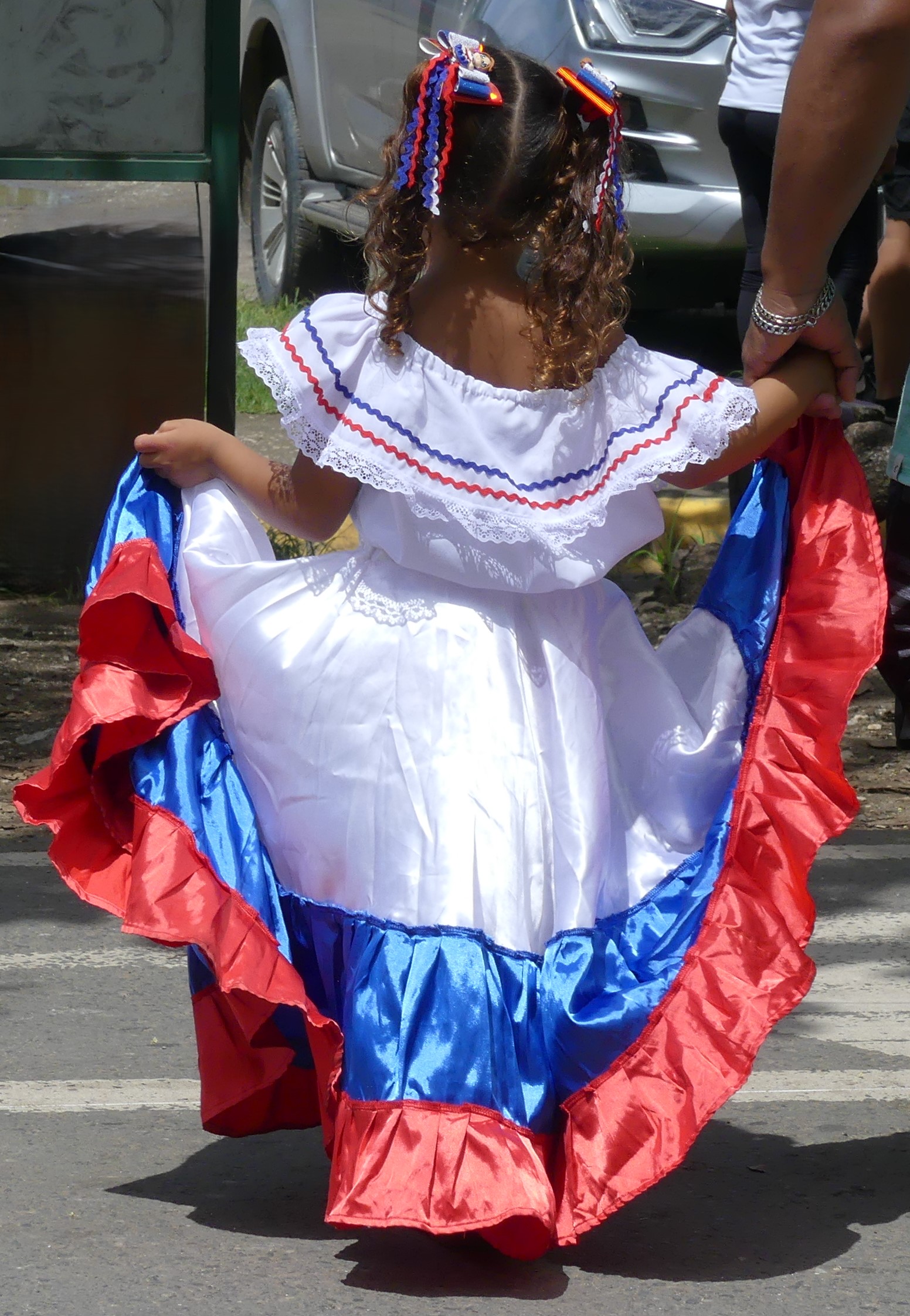 Petite fille de dos marchant main dans la main avec son père en tenue traditionnelle blanche bleue et rouge